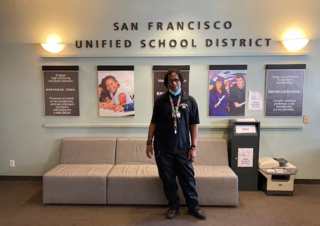 Tobias Cain, a security aide from Marshall Elementary School, poses in front of a wall at the SFUSD central office