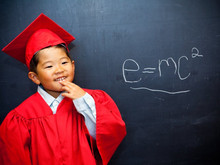 Early education student in hat and gown in front of blackboard