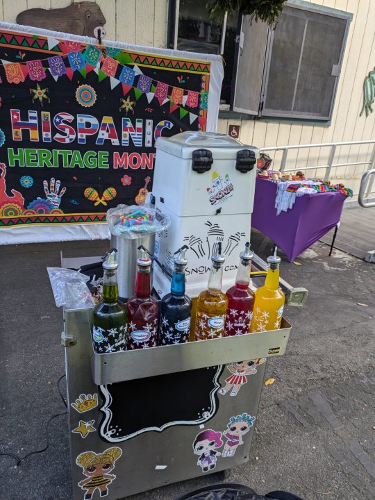 Snow cone machine set up for the event, hispanic heritage month poster set up behind it.