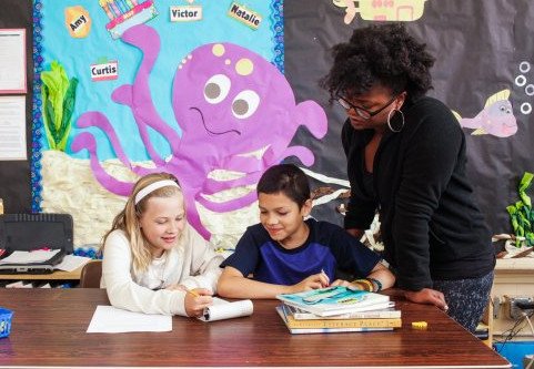 Teacher assisting two students at desk