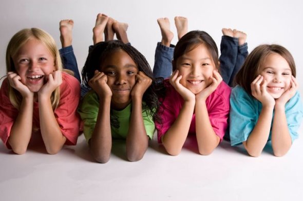 Four girls laying on their stomach, smiling with their heads in their hands and their barefeet lifted up behind them.