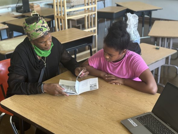 Photo of an adult reading along with a child in a pink shirt