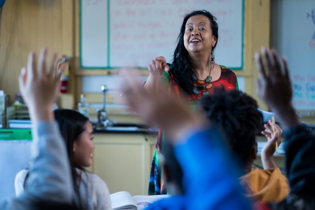 Teacher facing students with hands raised