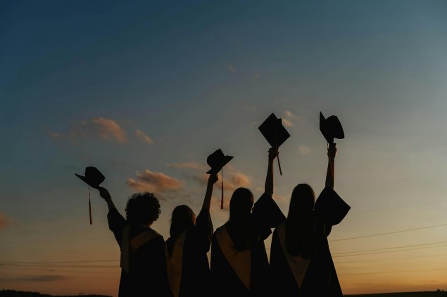 Students holding graduation cap in sunset