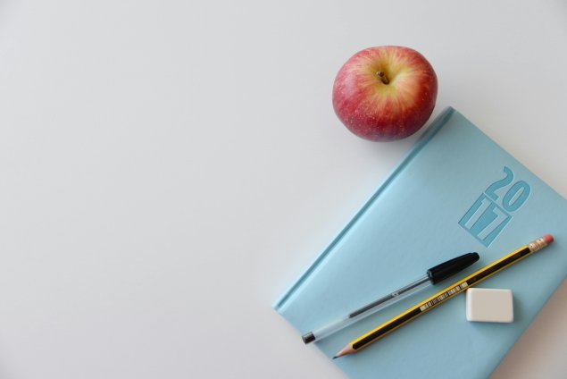 notebook with pen pencil, and eraser on top and apple on side